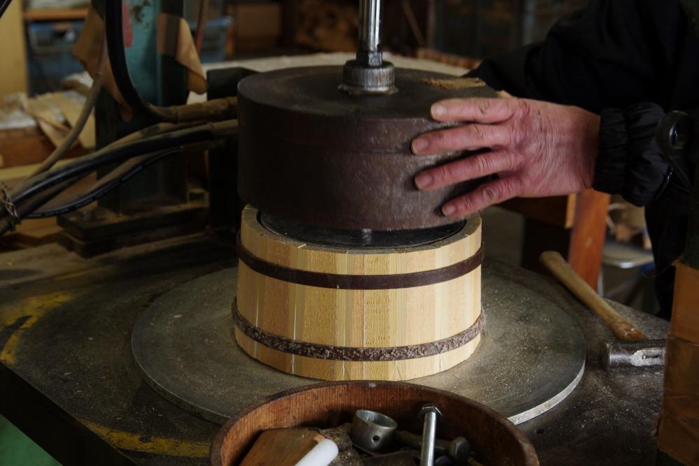  ▲側材の接着を強度にするため、上の仮タガを機械の圧力を借りて真ん中まで下していきます。